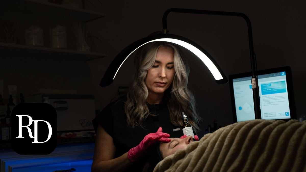 Woman getting a tattoo with a tattoo artist and computer setup in a dark room.